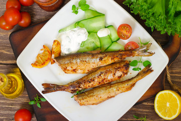 Roasted sardines with a salad of cucumber and yogurt on a wooden background.  Mediterranean cuisine