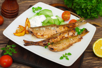Roasted sardines with a salad of cucumber and yogurt on a wooden background.  Mediterranean cuisine
