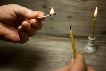 A lighted match in his hand and the candle, Matches with blue heads on wooden background