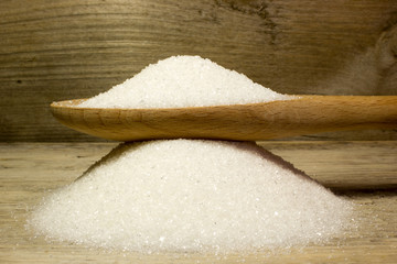Sugar and wooden spoon on wooden background