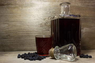 Glass and carafe with red alcoholic beverage, dried black berries of the bird cherry. The wood...