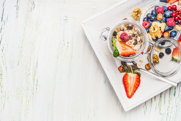 Fototapeta na wymiar Healthy breakfast preparation: Muesli in jar with summer fresh berries, seeds and nuts on light wooden background, top view,place for text