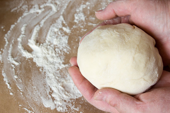The dough in his hands on the table with flour.