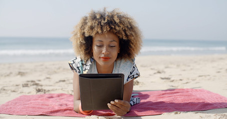Woman lying on beach towel and using a tablet computer on a beach
