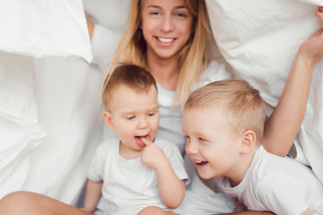 Two brothers playing with mother in bed.