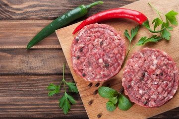 Raw beef cutlets with spices, rustic dark wooden background