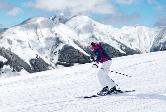 Colorful image of female skier sliding down the slope with panoramic winter mountains background
