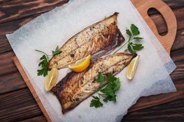 Grilled fish with herbs and lemon on rustic dark wooden background