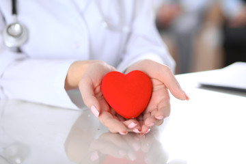 Female doctor with stethoscope holding heart.  Patients couple sitting in the background