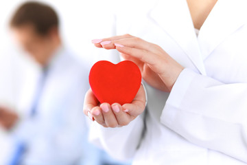 Femail doctor holding a red heart in his hands on a background of the patient. Health care concept