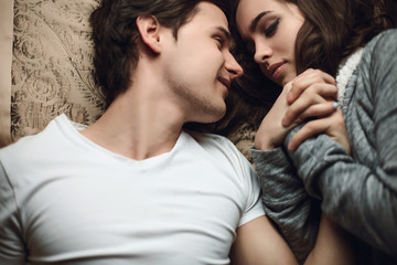 beautiful brunette girl and guy lying in bed and holding tightly hands. The concept of tenderness...
