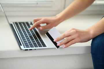 Fototapeta na wymiar Happy woman doing online shopping at home . Close- up of a hand holding a credit card next to a laptop
