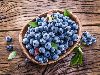 Ripe blueberries in the bowl on the wooden table.