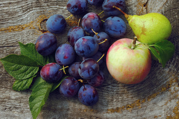 Plums, pear and apple on a wooden background. Fresh autumn crop of fruit.