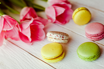 A beautiful bouquet of pink tulips with colorful macaroons on white wooden background