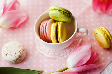 A beautiful flowers pink tulips with colorful macaroons laid in cup on white wooden background with pink Lacy napkin