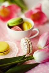 A beautiful flowers pink tulips with colorful macaroons laid in cup on white wooden background with pink Lacy napkin
