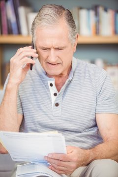 Senior man talking on mobile phone while looking documents