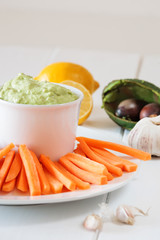 Fresh guacamole with carrot slices on a white wooden table