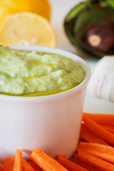 Fresh guacamole with carrot slices on a white wooden table