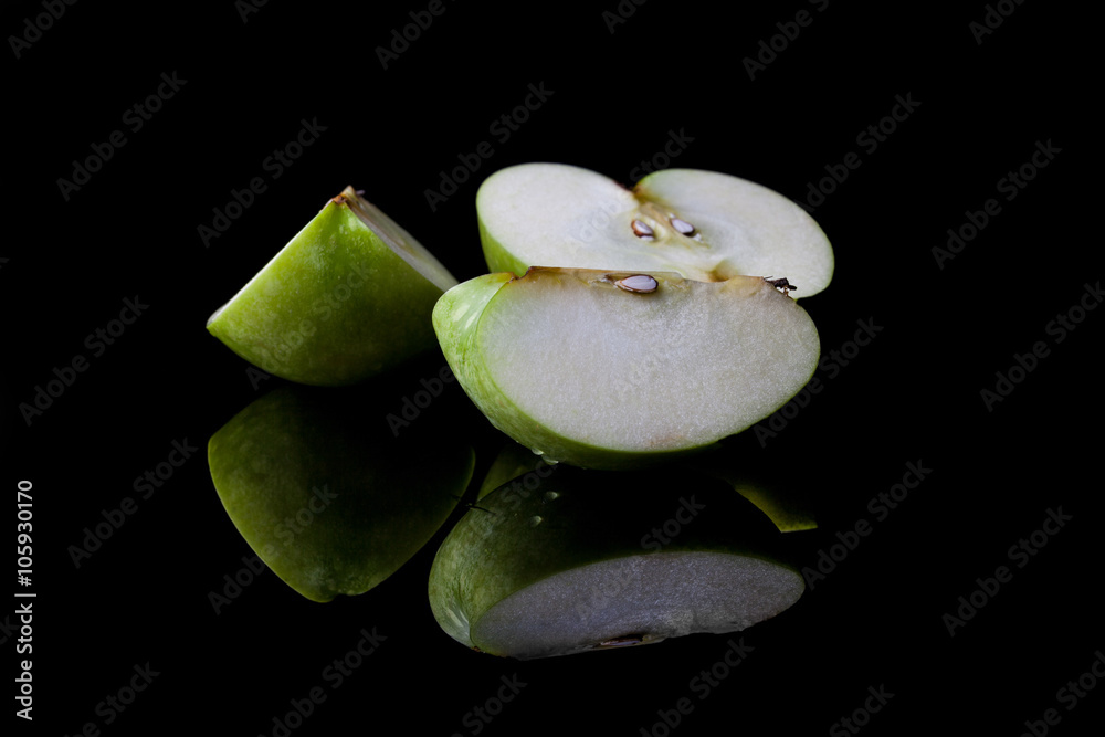 Wall mural sliced green apple half and two quarters on black background from side with reflection