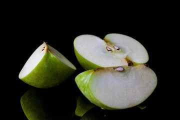 Sliced green apple half and two quarters on black background from side