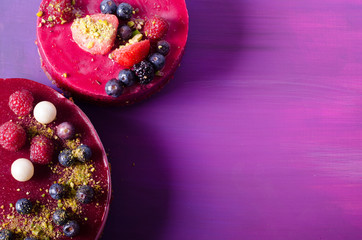 Two delicious cakes with fresh berries, raspberries, blueberry, currants and pistachios on bright background. Free space for your text.