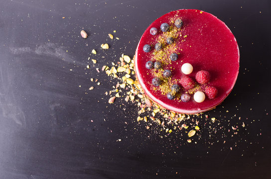 Delicious raspberry cake with fresh strawberries, raspberries, blueberry, currants and pistachios on black background. Free space for your text.