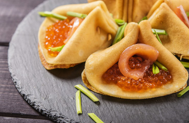Crepes stuffed with red caviar and salmon, sprinkled with green onions on a shale plate    