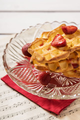 Cottage cheese waffles with strawberry sauce and a strawberry in a vase of glass on a red napkin and sheet music notation 