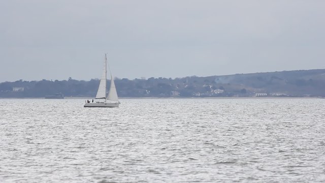 Sailing boat sails past coast.