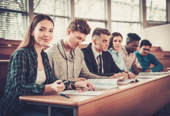 Multinational group of cheerful students taking an active part in a lesson while sitting in a lecture hall.
