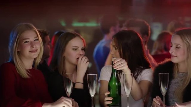 four attractive girls at bar in club are about to open a bottle of champagne