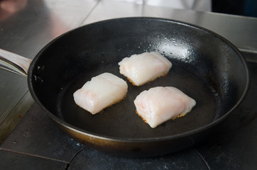 Pan fried golden fish fillet cubes, frying in real butter, in a non stick rustic pan.