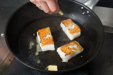 Pan fried golden fish fillet cubes, frying in real butter, in a non stick rustic pan.