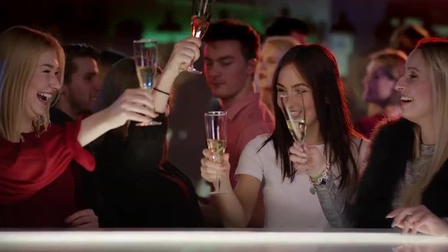 four attractive girls at bar in club raising their champagne glasses