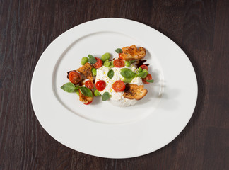 Delicious tomato and mozzarella cheese salad caprese, served on a white plate, with basil, croutons and balsamic vinegar.