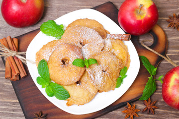 Apples fried in a batter with mint, cinnamon and powdered sugar on wooden table.
