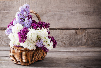 basket with a branch of lilac flower on a wooden background