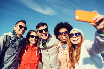 smiling friends taking selfie with smartphone