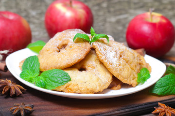 Apples fried in a batter with mint, cinnamon and powdered sugar on wooden table.