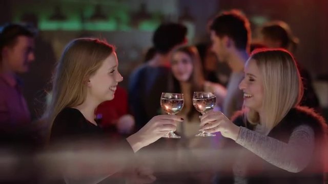 two attractive girls at bar in club raising their glasses