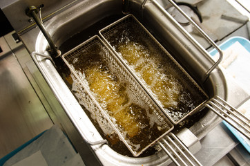 A silver deep pan industrial kitchen oil fryer, with golden oil, bubbling and frying potatoes