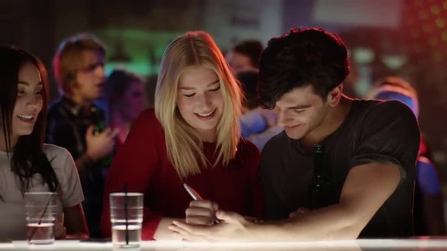 attractive blond girl at bar in club writing her phone number on hand of good looking guy