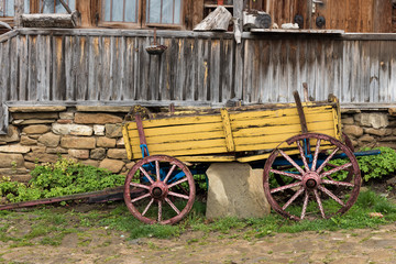 Fototapeta na wymiar Yellow wooden waggon in front of old house in Jeravna village