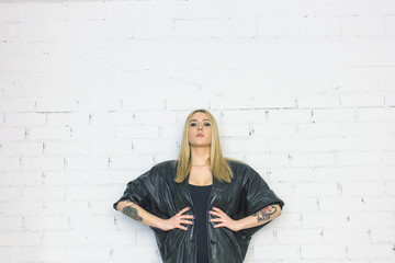 Blonde tattooed fashion girl on white bricks wall