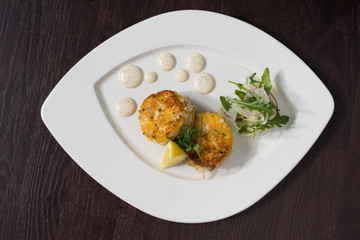 Beautiful fresh golden fish cakes, served with a wedge of lime, dill sauce and rocket on a white plate