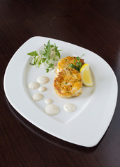 Beautiful fresh golden fish cakes, served with a wedge of lime, dill sauce and rocket on a white plate