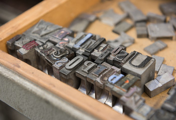 Vintage lead letterpress printing blocks against a weathered wooden drawer background with bokeh.