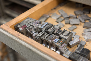 Vintage lead letterpress printing blocks against a weathered wooden drawer background with bokeh.